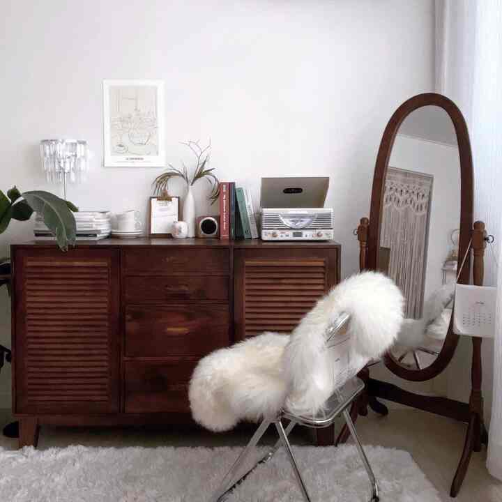 アイボリーとダークブラウンの木目調が特徴的な寝室、ヴィンテージの収納棚と全身鏡、ふわふわのラグが配置された雰囲気のあるインテリア