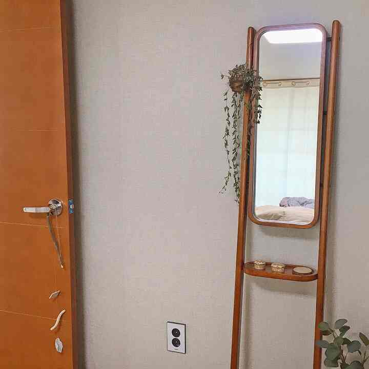 Natural beige-walled bedroom space featuring a wood-framed standing full-length mirror with warm ambiance
