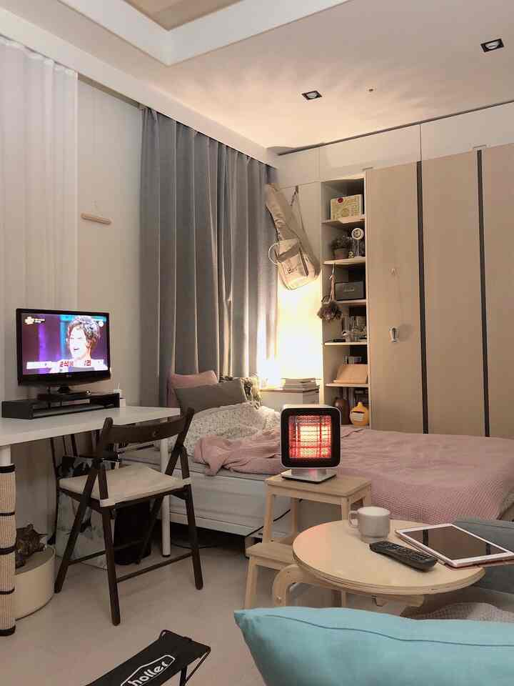 Studio bedroom with gray curtains and pink bedding, featuring an electric heater adding warmth to the cozy room