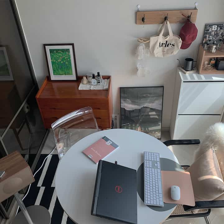 ホワイトとウッドトーンのワンルームホームオフィス、ラタンのアームチェアと効率的な収納キャビネットが配置されたナチュラルモダンな雰囲気のインテリア