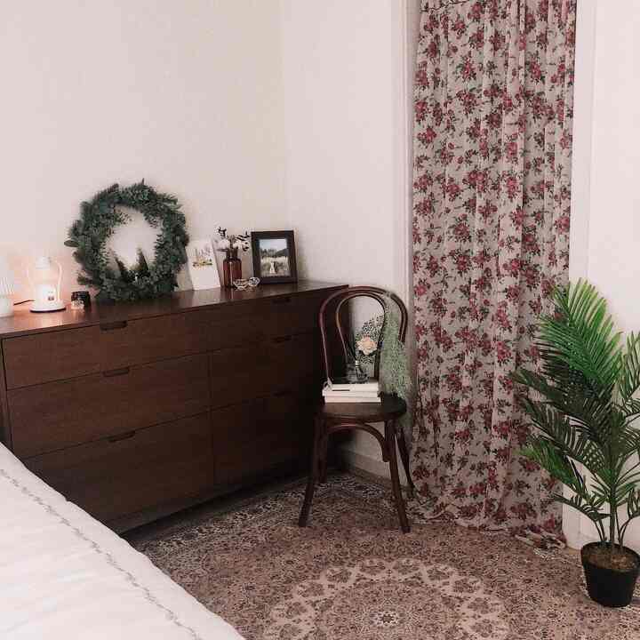 木目調の家具とヴィンテージ風のペルシャラグがある居心地の良い寝室、花柄のカーテンと緑の植物が配置された印象的な空間