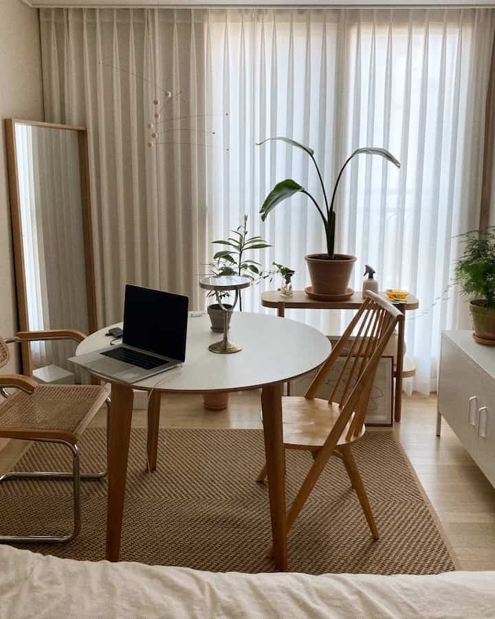 Bright white-toned dining room featuring wooden table and chairs, with various potted plants creating a natural and simple atmosphere