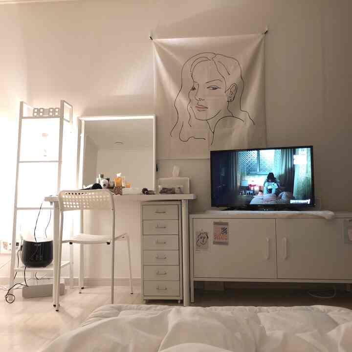 White-toned studio living room featuring dresser, TV stand, desk, and chair with a clean natural atmosphere