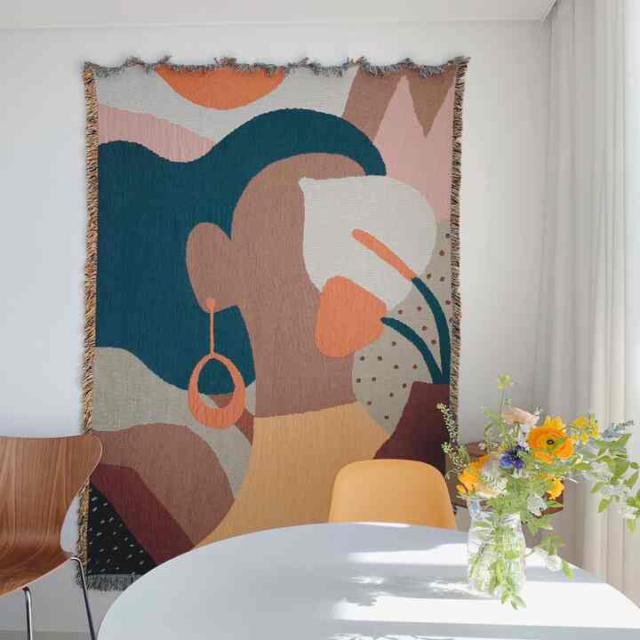 A cafe-style living room with a white background, featuring a round dining table, diverse colored chairs, and an art wall tapestry