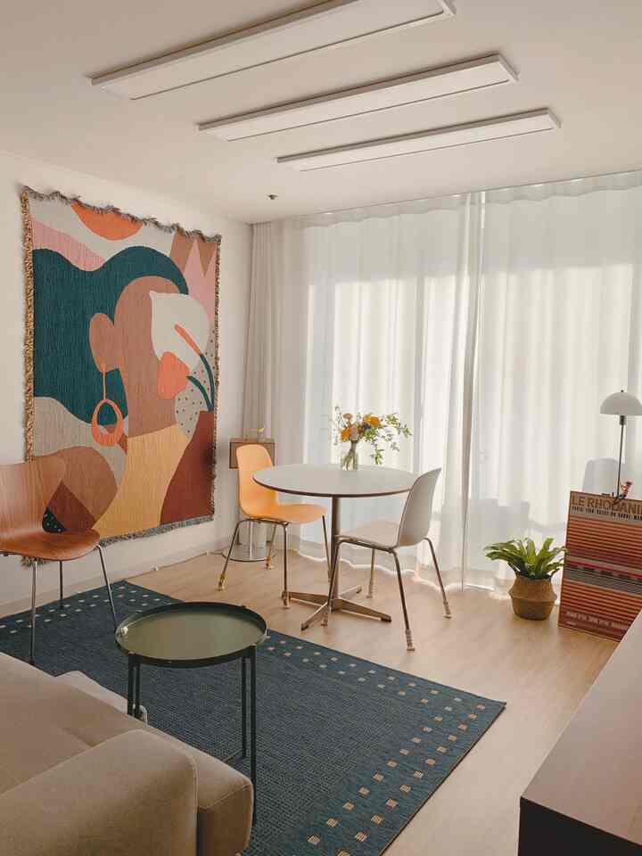 Natural-toned dining room featuring a round table with chairs, white curtains, and warm brown sofa creating a cozy atmosphere