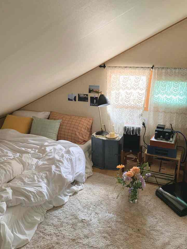 White and beige toned loft featuring a bed, nightstand, and lace curtains with warm atmosphere