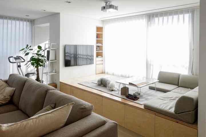 Natural-toned living room featuring a floor platform, sofas, and rug creating a cozy modern atmosphere