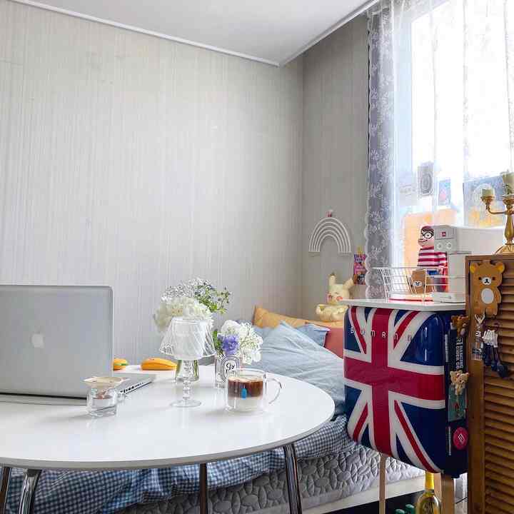 White-toned small single household room featuring a round table, mini fridge, and sofa bed with cozy home cafe atmosphere
