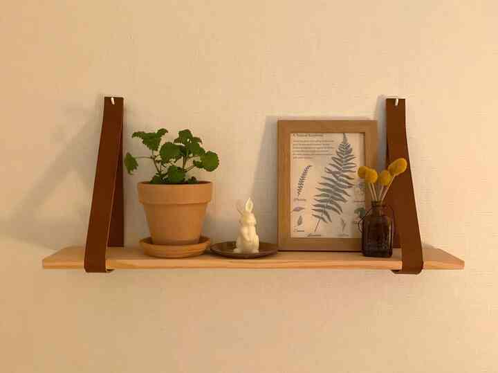 Natural tone studio apartment featuring a wooden shelf with terracotta plant pot, rabbit-shaped candle, picture frame, and dried flowers arranged charmingly