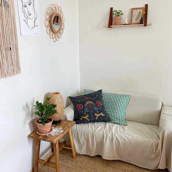 Bright beige-toned studio living room featuring natural wood stool, rattan mirror, and fabric sofa creating a cozy atmosphere