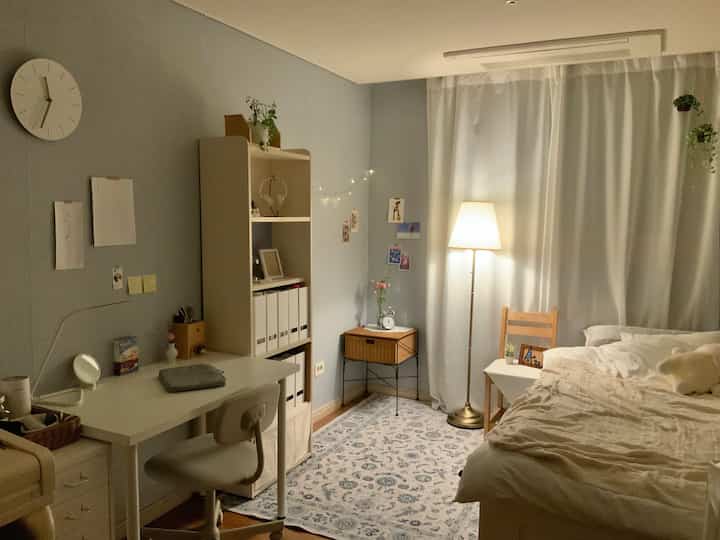 Soft blue and white bedroom featuring desk, rattan shelf, and cozy floor lamp with warm ambiance