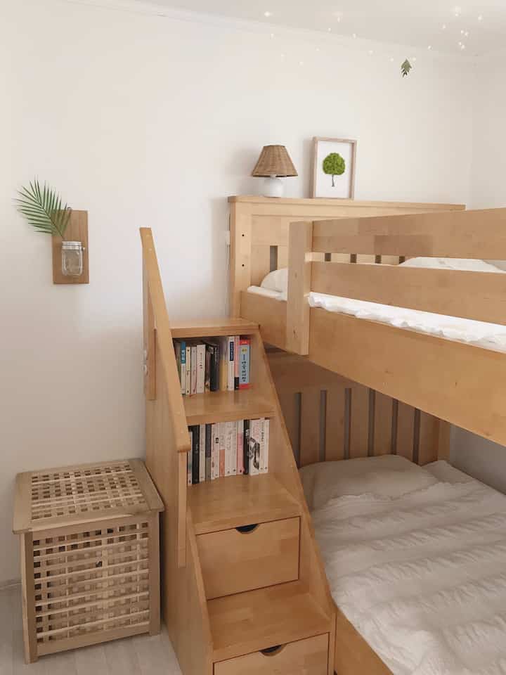 Bright wood tone and white kids' room featuring a bunk bed with storage stairs, clean and natural atmosphere