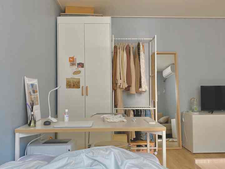 スカイブルーの壁紙が印象的な一人暮らしの寝室、ホワイトの家具とベージュトーンのハンガーが配置されたミニマルな空間