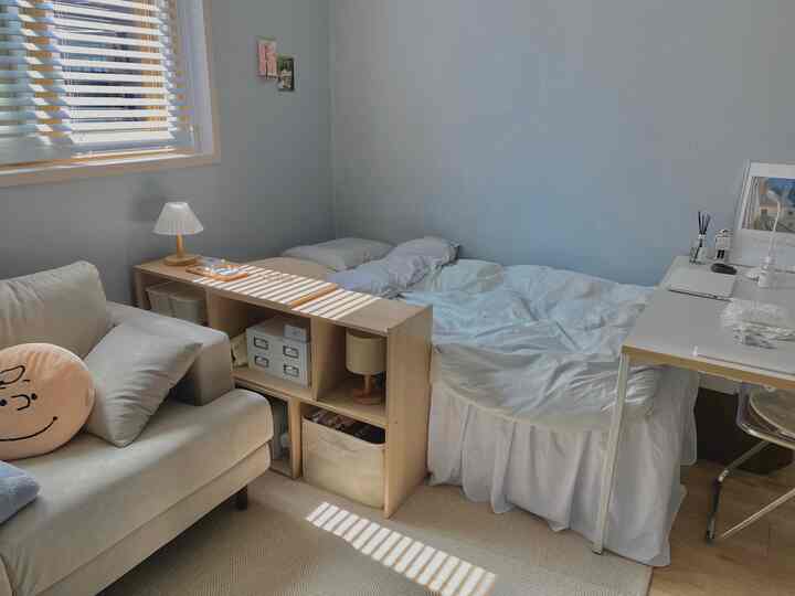 ホワイトとグレーの色調のワンルーム寝室、デスクとソファが配置され、自然光が差し込む印象的な空間