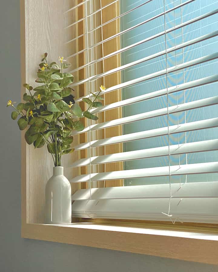 白いブラインドと木目調の窓枠がある窓際に、白い花瓶に入ったユーカリの造花が置かれた、温かみのあるナチュラルな空間