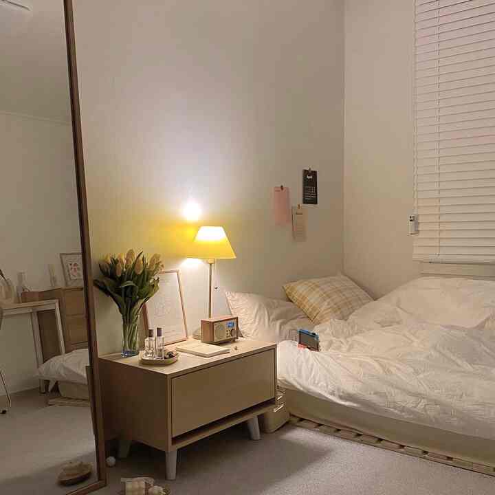 白と木目調の調和が取れた寝室、ナイトテーブルの上にテーブルランプと全身鏡が配置されたシンプルで温かみのある自分の部屋