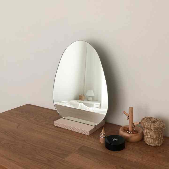 Natural-tone wall and wood-toned vanity table with a simple-shaped frameless mirror placed in a clean space