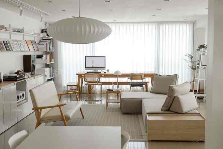 Bright white and light brown toned living room featuring large sofa, armchair, desk, and shelves in a natural modern style