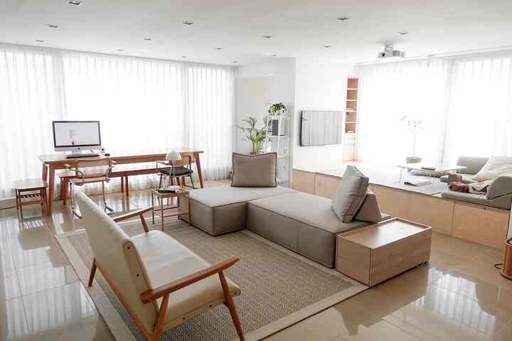 Bright natural-toned living room featuring beige fabric sofa, wood-tone floor seating area, and computer desk creating an open atmosphere