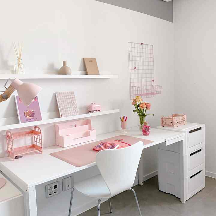 A clean study space in white and pink tones, featuring a desk and storage units arranged for convenience in a cozy hobby room