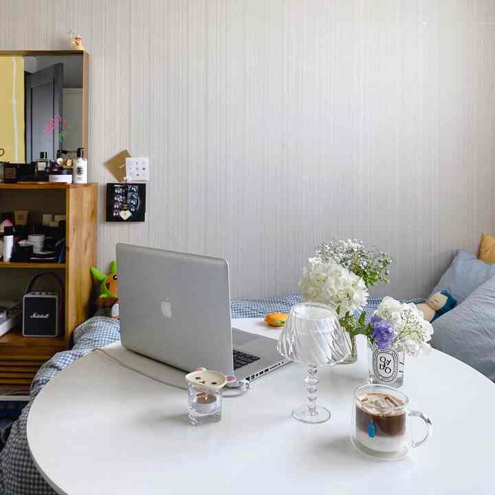 White and blue toned bedroom featuring a round table with laptop, vases, and coffee for a cozy home office and home cafe setup