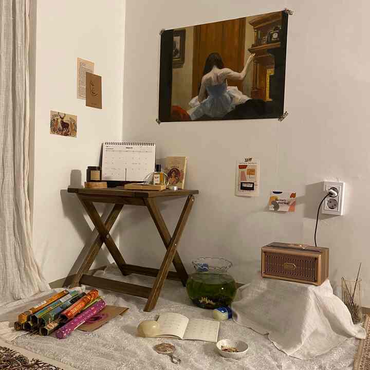 A studio apartment with white walls and wood-tone furniture, featuring vintage art and a folding stool repurposed as a nightstand, creating a cozy atmosphere