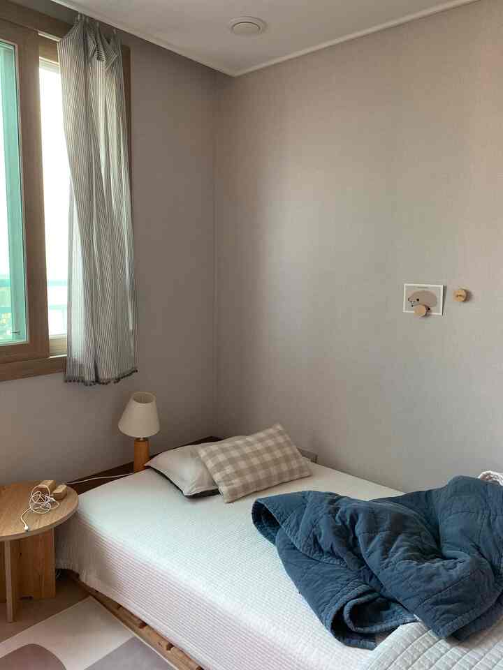 Soft white and natural brown toned small bedroom featuring a simple single bed and wooden side table, creating a cozy atmosphere