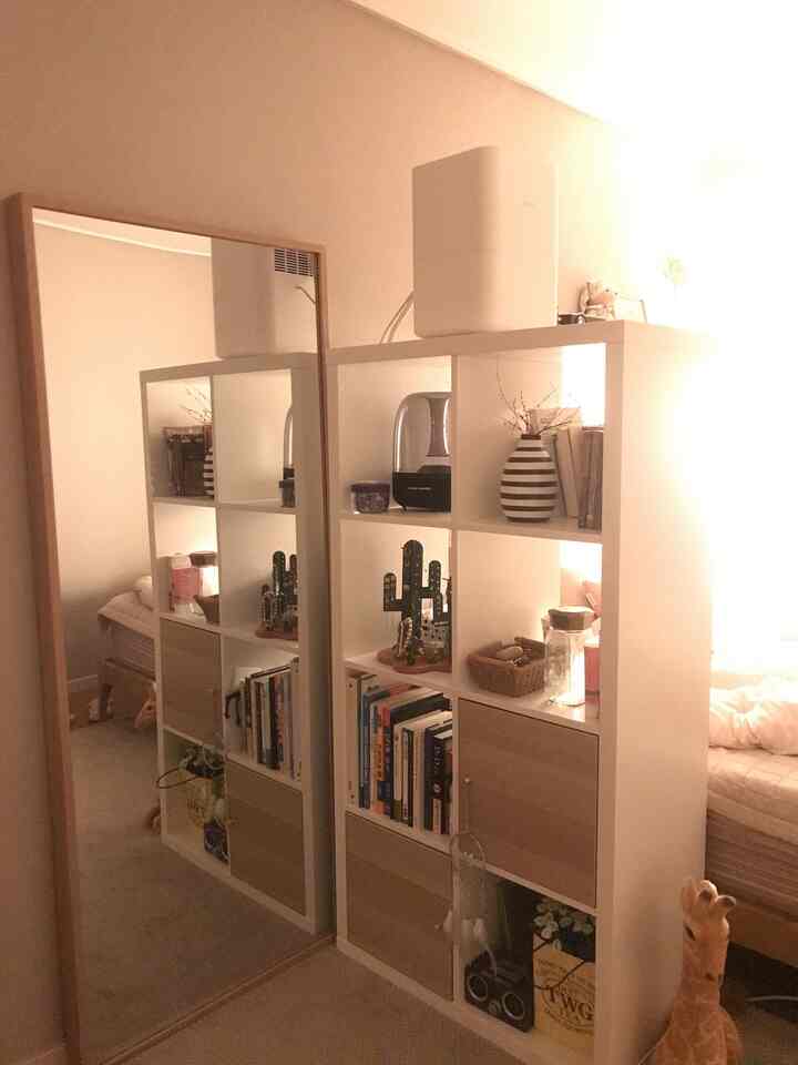 White and beige toned bedroom featuring a full-length mirror and bookshelf creating a cozy atmosphere
