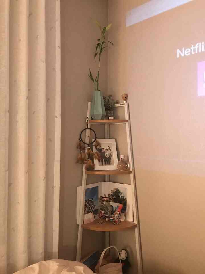 Beige-toned bedroom corner storage space featuring a major corner shelf with dreamcatcher decor and projected home cinema screen, cozy atmosphere