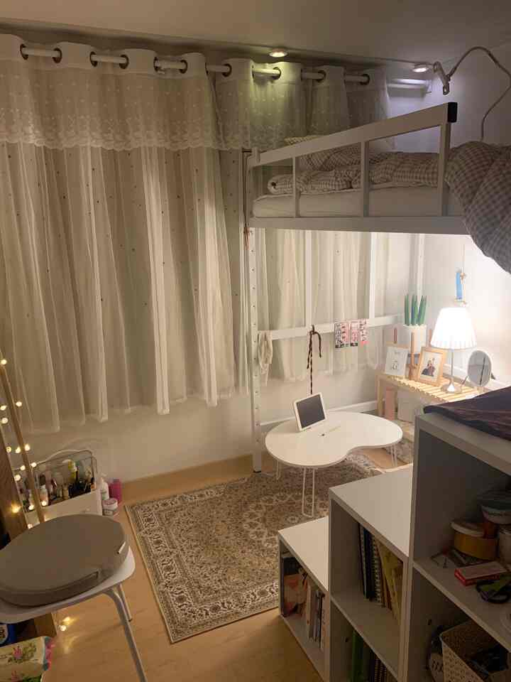 White-toned small bedroom featuring a white loft bed, floral patterned rug, and sheer curtains creating a cozy atmosphere