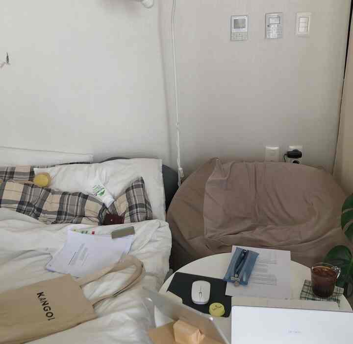 白とベージュのトーンの狭い寝室、ベッドとビーズクッション、作業テーブルが配置された落ち着いた雰囲気のインテリア