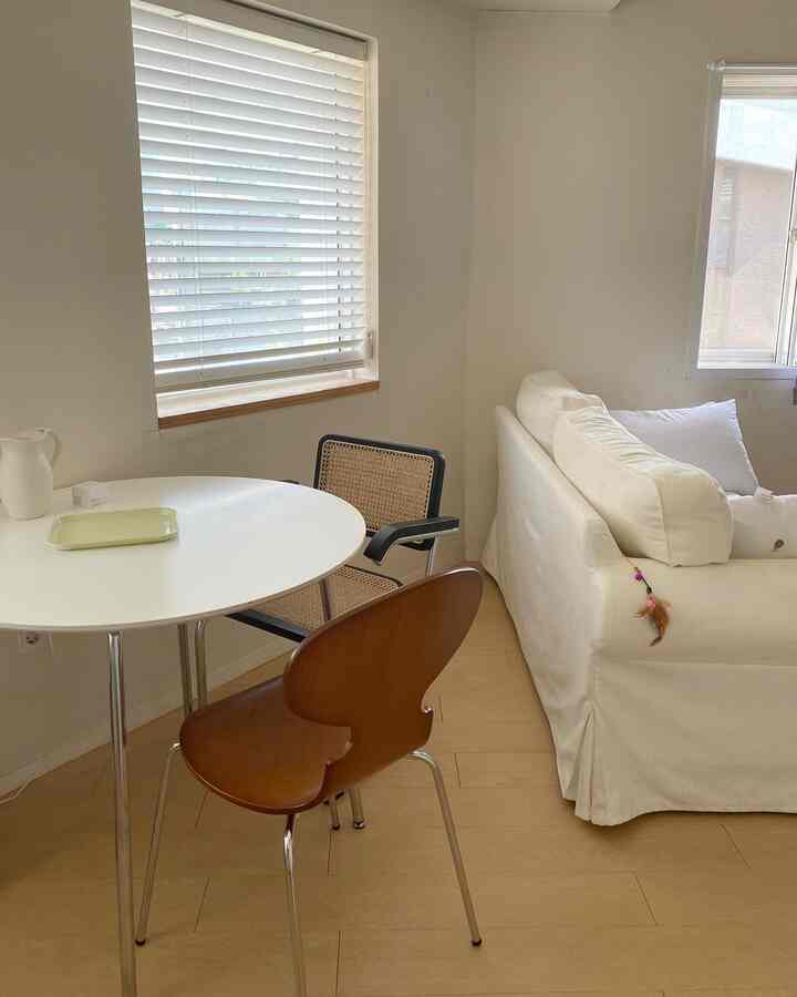 A living room featuring white and natural color tones, with a simple dining table and chairs arranged in a cozy setting