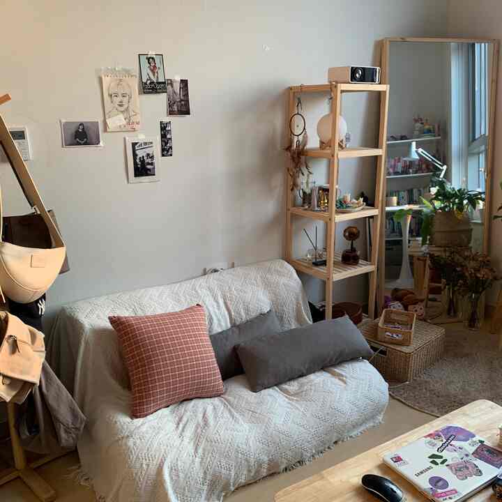 ホワイトとウッドトーンのワンルームリビング、ソファと棚、大型の鏡が配置された雰囲気のあるインテリア