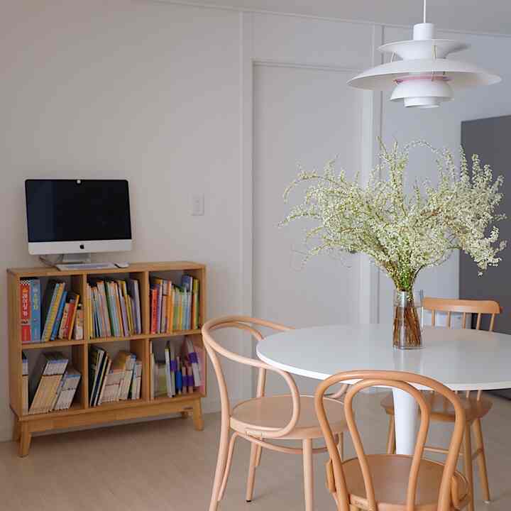 White and wood tone kitchen dining area featuring round dining table, kid's bookshelf, and pendant light with a bright natural atmosphere