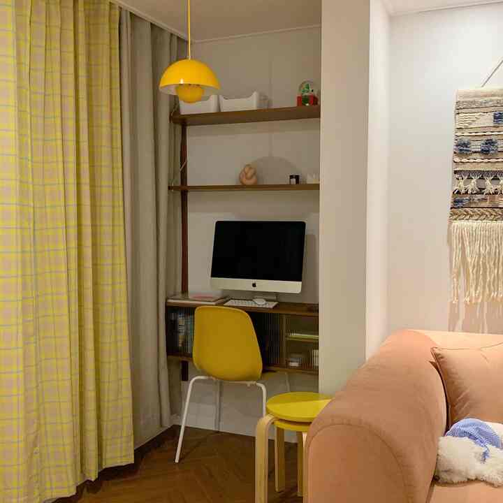 Yellow-accented small study space featuring a desk with computer and yellow chair beside a cozy peach sofa in living room corner