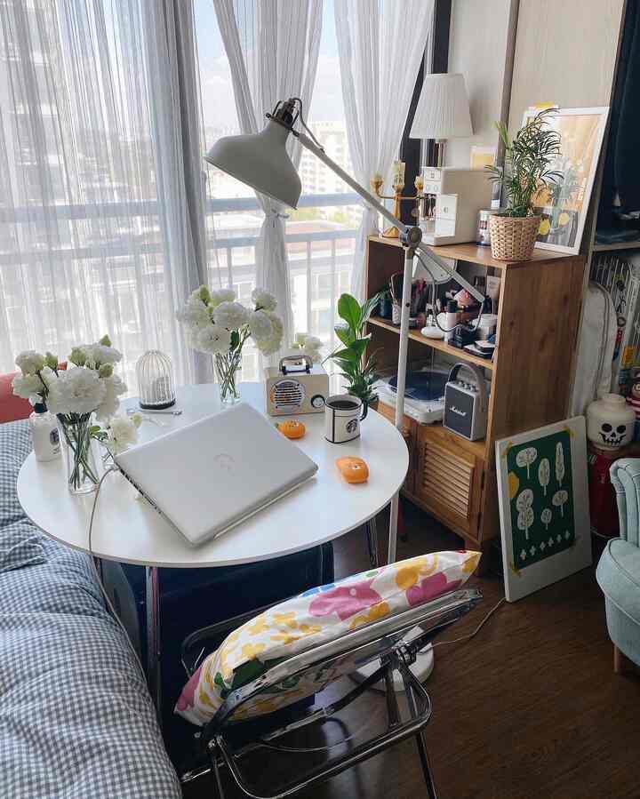 白を基調としたコンパクトなホームオフィス、丸テーブルとフロアランプ、植物が配置された雰囲気のあるインテリア