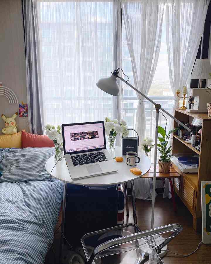 White and brown toned studio apartment home office featuring a round table, transparent chair, and wooden shelves creating a cozy atmosphere