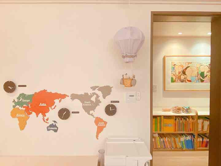 白い壁と木目調の本棚が配置された子供部屋で、カラフルな世界地図のウォールデコとおもちゃ収納が印象的な雰囲気のあるインテリア
