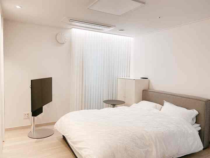 ホワイトとナチュラルカラーの寝室、シンプルなベッドとテレビスタンドが配された落ち着いたインテリア