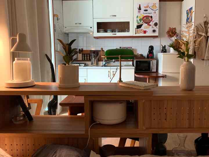 温かみのあるナチュラルな木目調と白が調和するワンルーム、テーブルライトと植物が配置された雰囲気のある空間