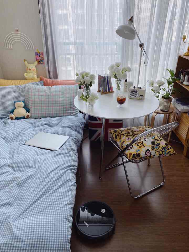 A white and brown toned studio bedroom featuring tidy bedding, a round table, and plants, creating a cozy atmosphere