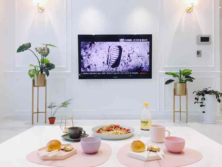 ホワイトとゴールドのトーンでまとめられたリビング、中央のテーブルには2人分のブランチセットと左右にグリーンの植物スタンドが配置された雰囲気のあるインテリア