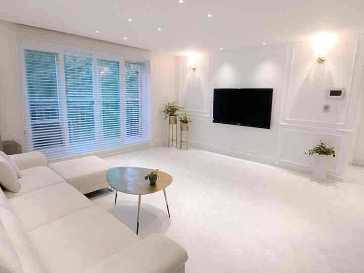 A sleek living room in white with gold accents, featuring a spacious clean sofa and wall-mounted TV