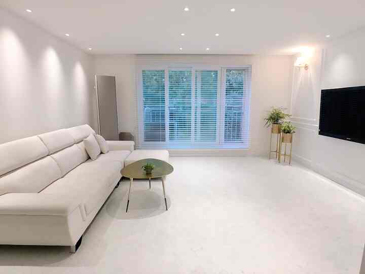 ホワイトとゴールドの色調が美しい、シンプルで広々としたリビング。最小限の家具と壁掛けテレビが配置されたモダンなインテリア