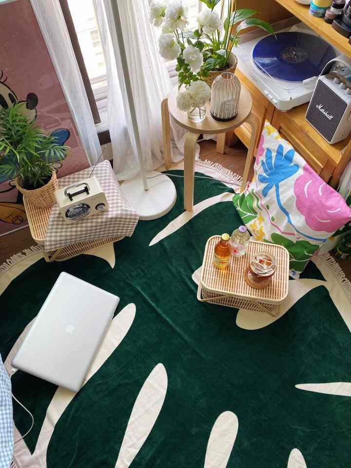 ホワイトカーテンと木目調の家具が配置された小さな部屋、グリーンの葉柄ラグとレトロなスピーカーがある雰囲気のあるインテリア