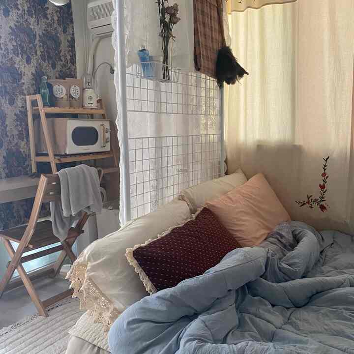 Warm natural toned studio apartment featuring vintage furniture, curtains, and a mesh room divider creating a cozy bedroom space