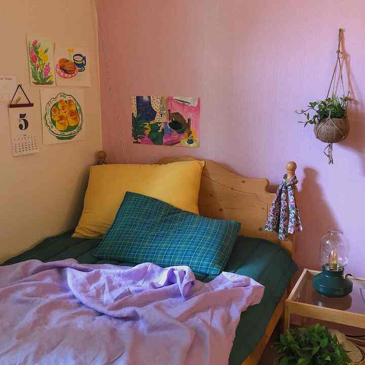 Bedroom with pink and lavender wallpaper, wooden bed with yellow and green pillows, and hanging plant creating a cozy atmosphere