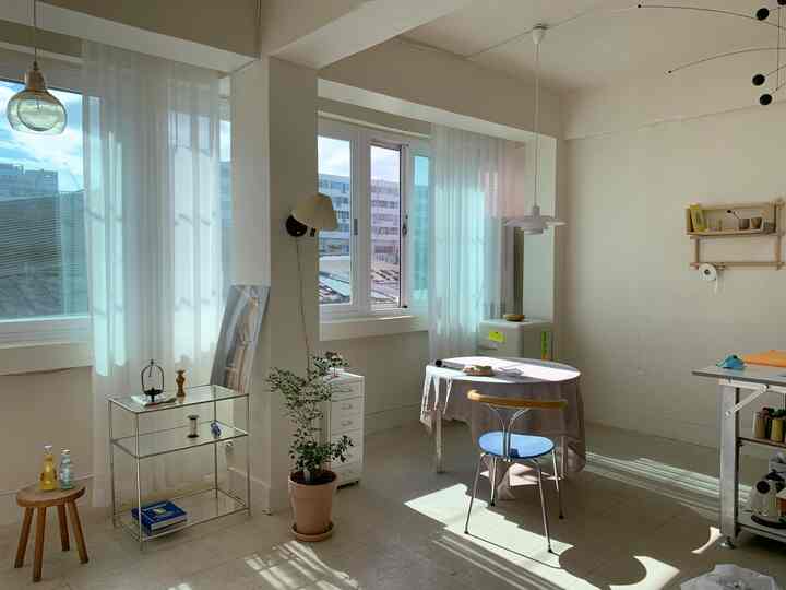 白とナチュラルな色調のコンパクトな部屋、丸テーブルと椅子、チェストと植物が配置された清潔感のあるインテリア