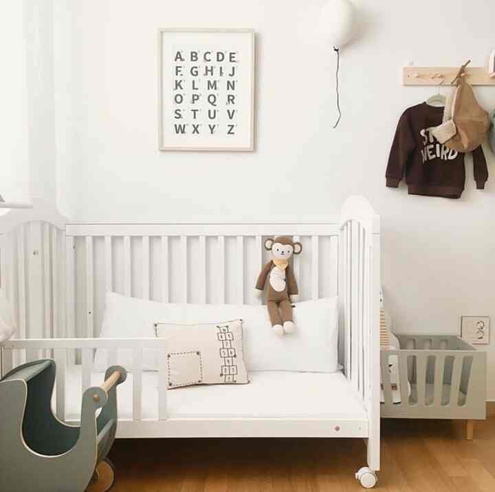 白とナチュラルカラーの子供部屋、ベビーベッドソファとクッション、ぬいぐるみが配置された雰囲気のあるインテリア