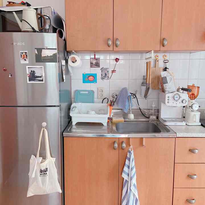 木目調のキャビネットと白いタイル壁のキッチンに、コーヒーマシンとタオルが配置された清潔感のある空間